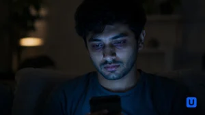 A tired person staring at a smartphone screen in a dark room representing Silent Scrolling Syndrome and Mobile Addiction.